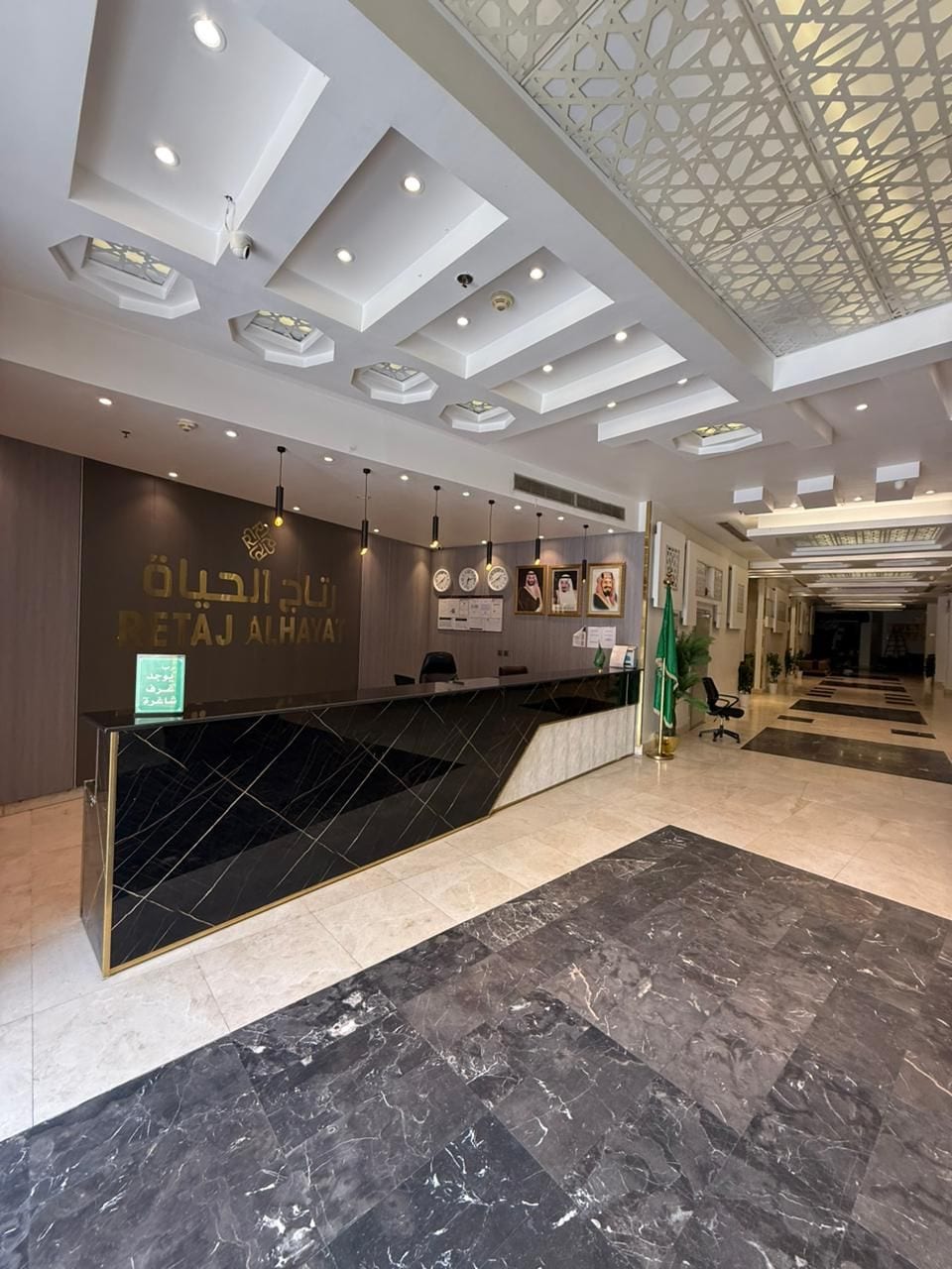 Zona de recepción de un hotel con diseño moderno, que incluye un mostrador de recepción, un reloj en la pared e iluminación empotrada en el techo.