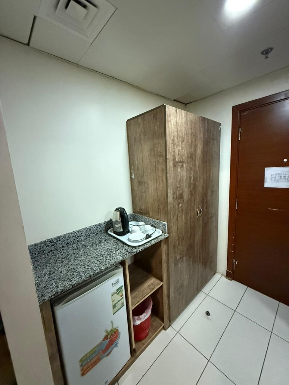 A compact kitchenette with a refrigerator, a wooden cabinet, and a countertop with a kettle.