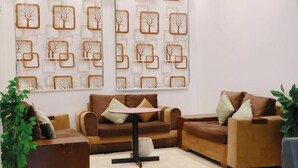 A modern living room with a brown sofa set, a small round table, and decorative wall art featuring geometric shapes and tree designs. - Retaj Hotel (Makkah)