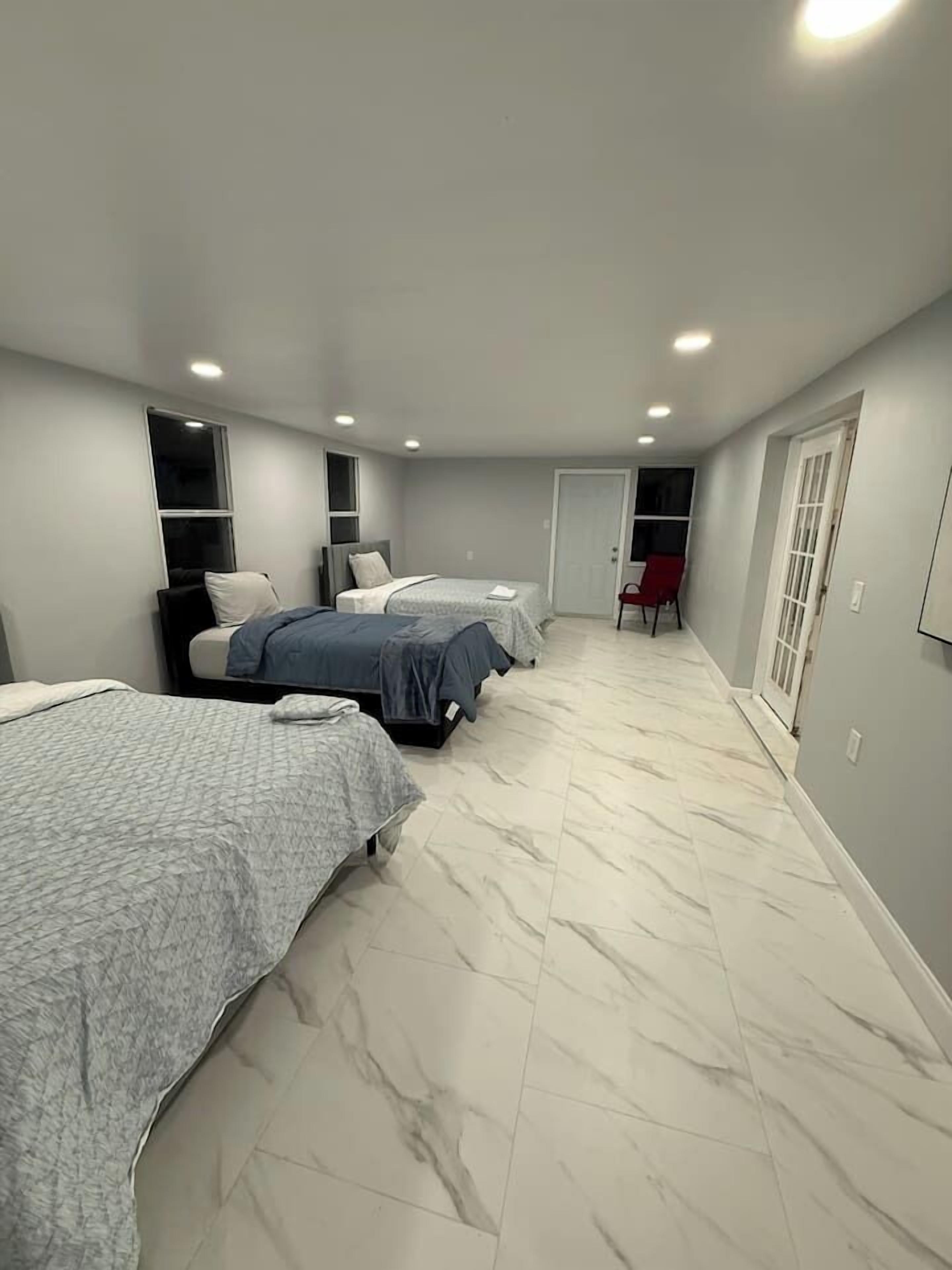 Une chambre avec deux lits, un fauteuil rouge et une porte qui donne sur une autre pièce.