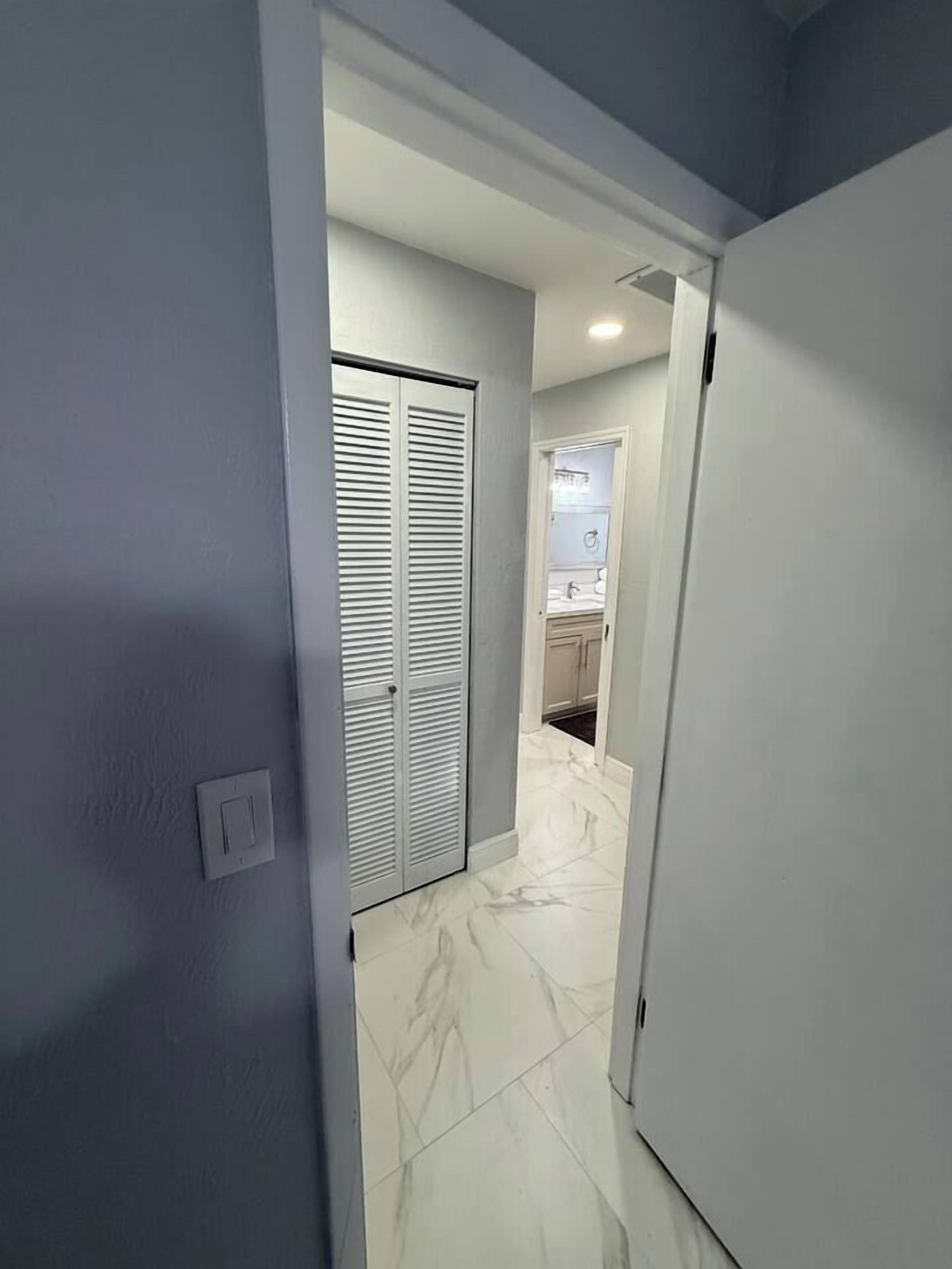 A hallway with a closed door, a light switch, and a bathroom with a sink and mirror.