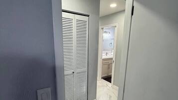 A hallway with a closed door, a light switch, and a bathroom with a sink and mirror.