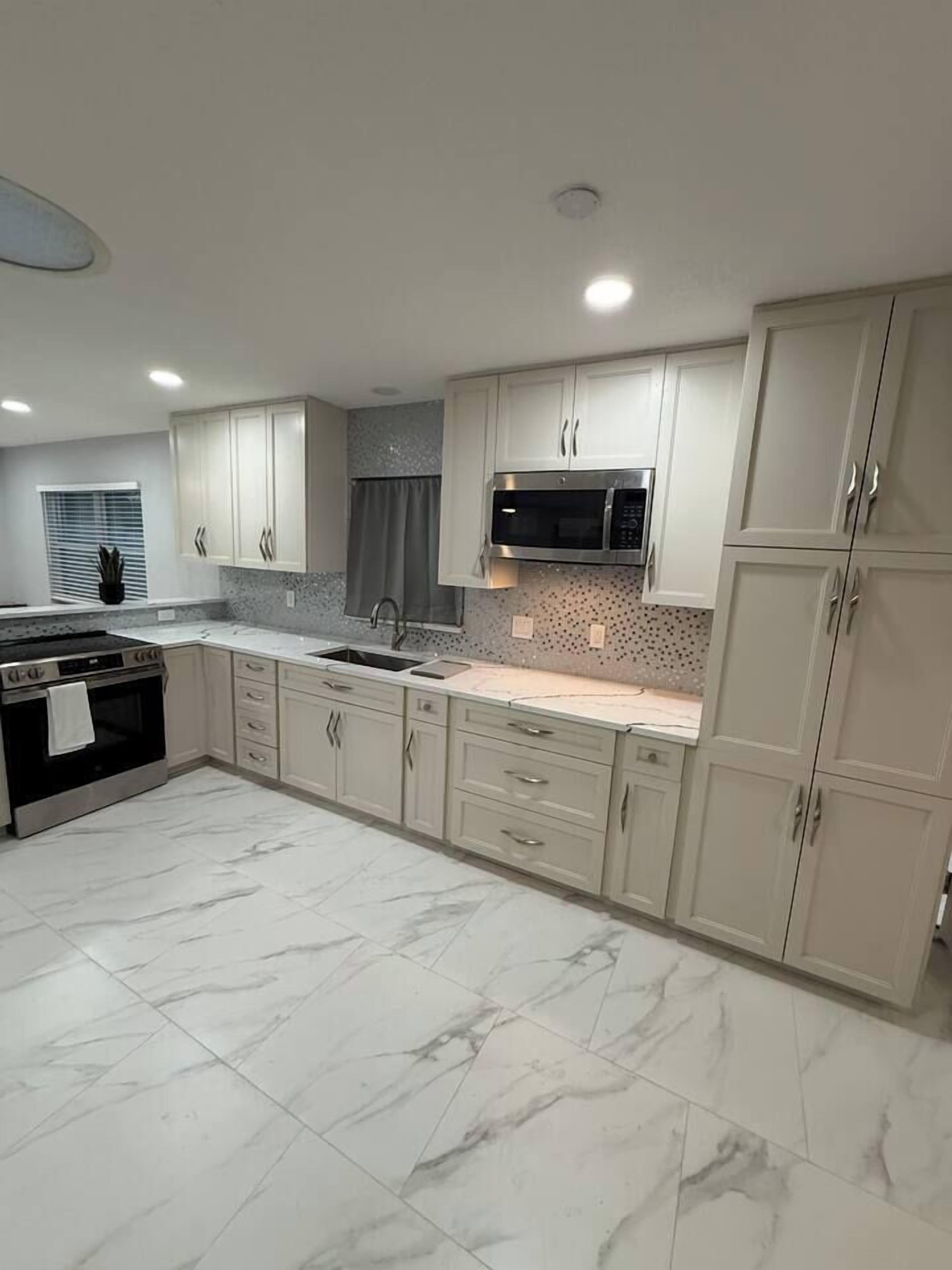 A modern kitchen with marble flooring, stainless steel appliances, and light-colored cabinetry.