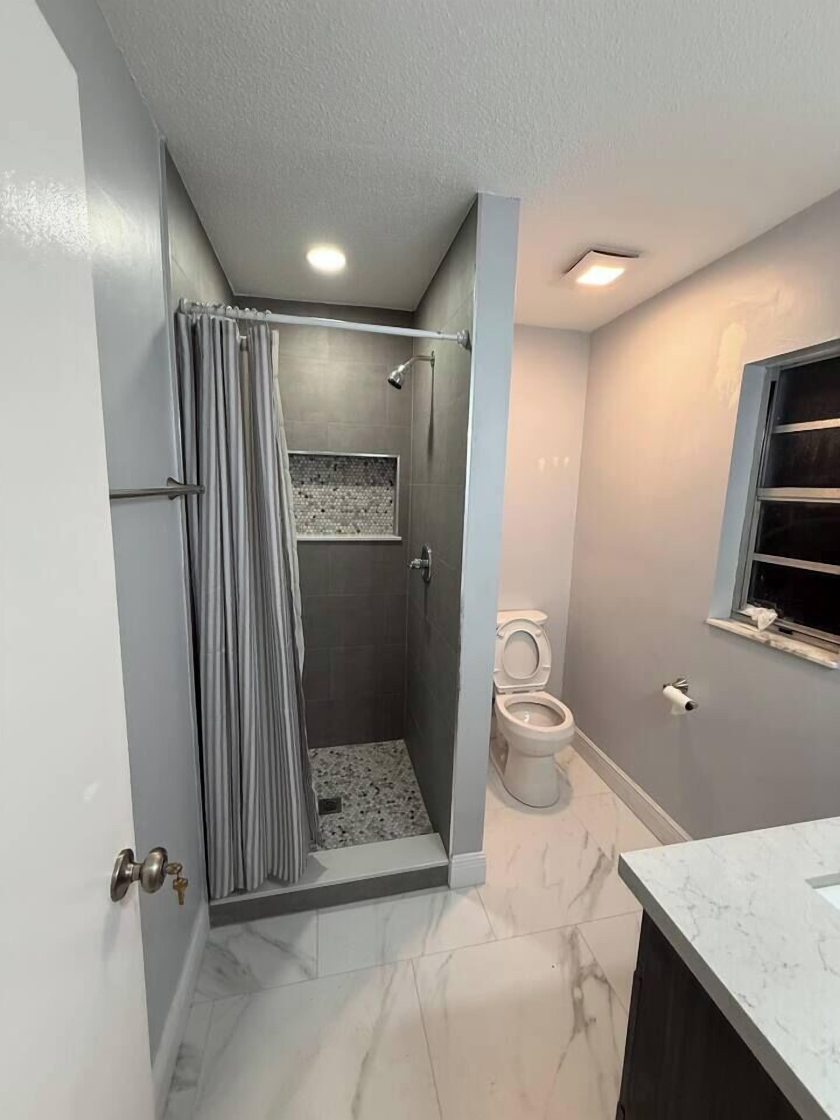 A bathroom with a shower, toilet, and a marble-tiled floor.