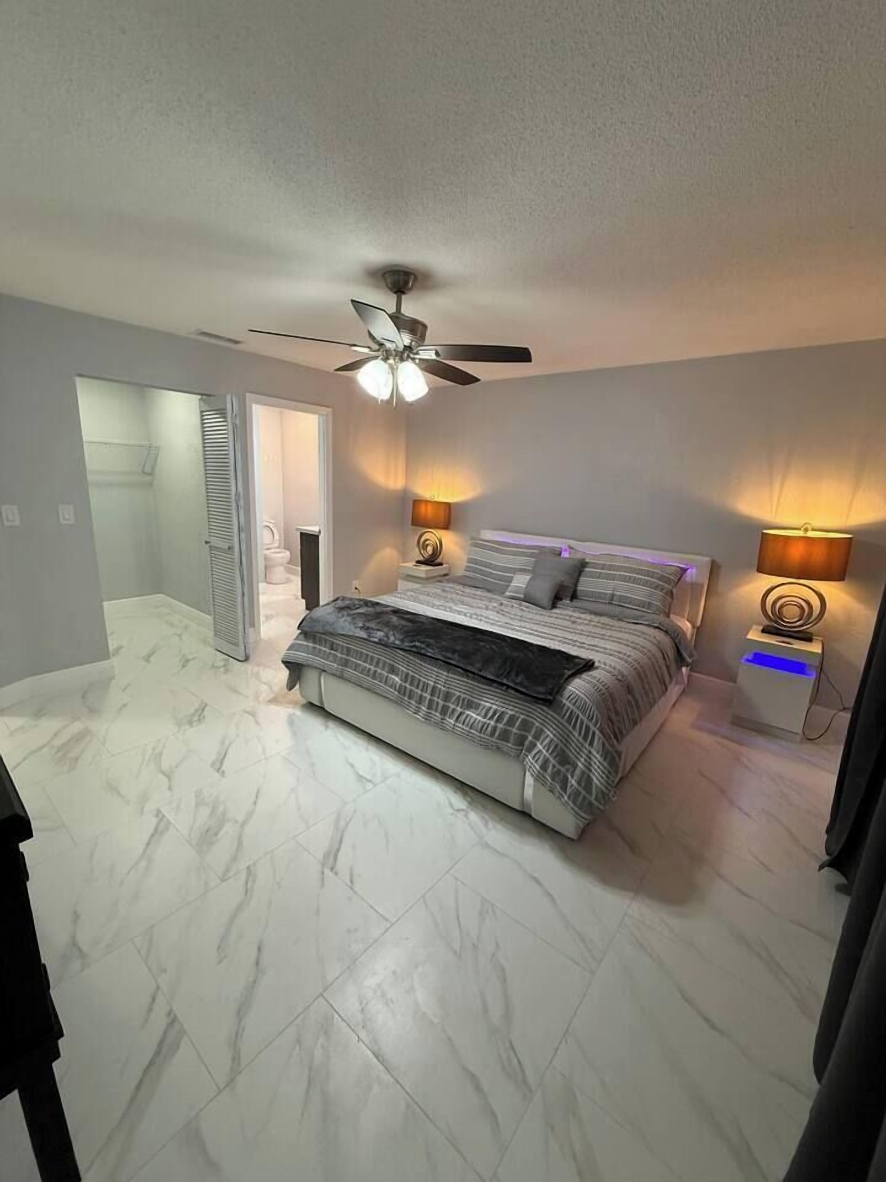 A bedroom with a bed, bedside lamps, a ceiling fan, and a bathroom door.
