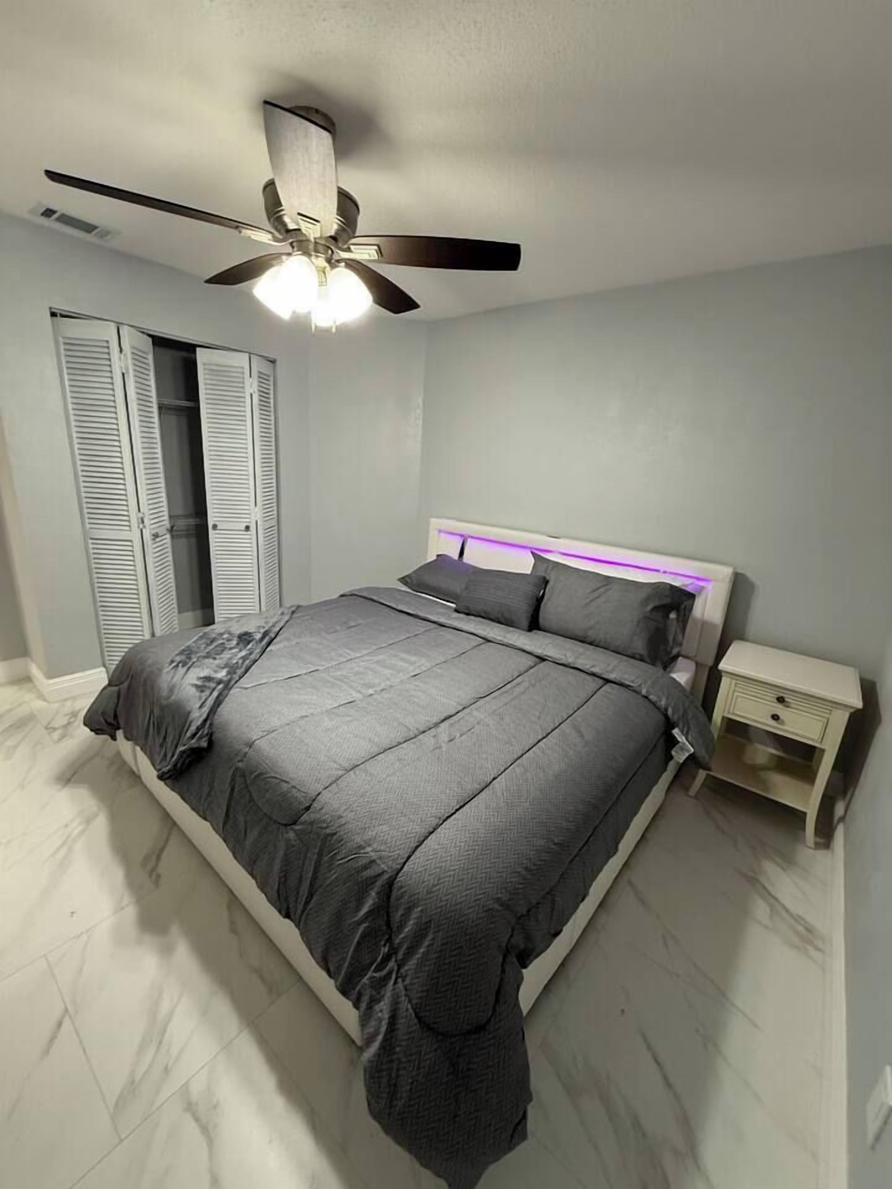 A bedroom with a bed, a nightstand, a ceiling fan, and a wardrobe with sliding doors.