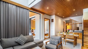 A modern living room with a sofa, armchair, and coffee table, a dining area with a table and chairs, and a kitchen with wooden cabinets and a stove. - Kanasu Villa by Exotic Bali Properties (Canggu)