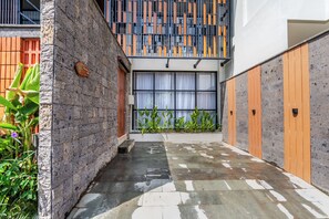 A modern building with a stone facade, a wooden door, and a window with curtains. - Kanasu Villa by Exotic Bali Properties (Canggu)
