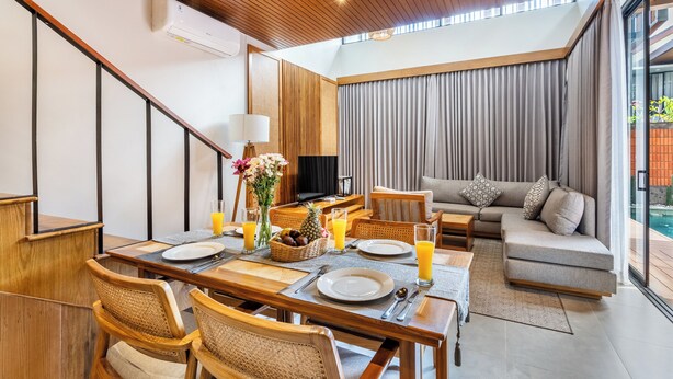 A modern living room with a dining area, featuring a wooden ceiling, a flat-screen TV, a sofa, and a view of the outdoors. - Kanasu Villa by Exotic Bali Properties (Canggu)
