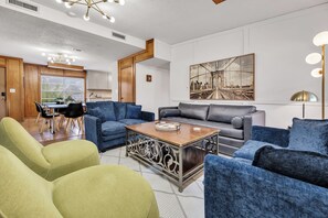 Una sala moderna con sofás azul y verde, una mesa de centro y un cuadro de gran formato con un paisaje urbano en la pared.