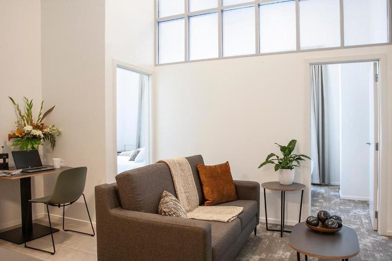 A modern living room with a sofa, a coffee table, a desk with a laptop, and a potted plant.