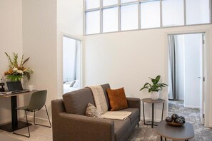 Una sala de estar moderna con un sofá, una mesa de centro, un escritorio con una computadora portátil y una planta en maceta.