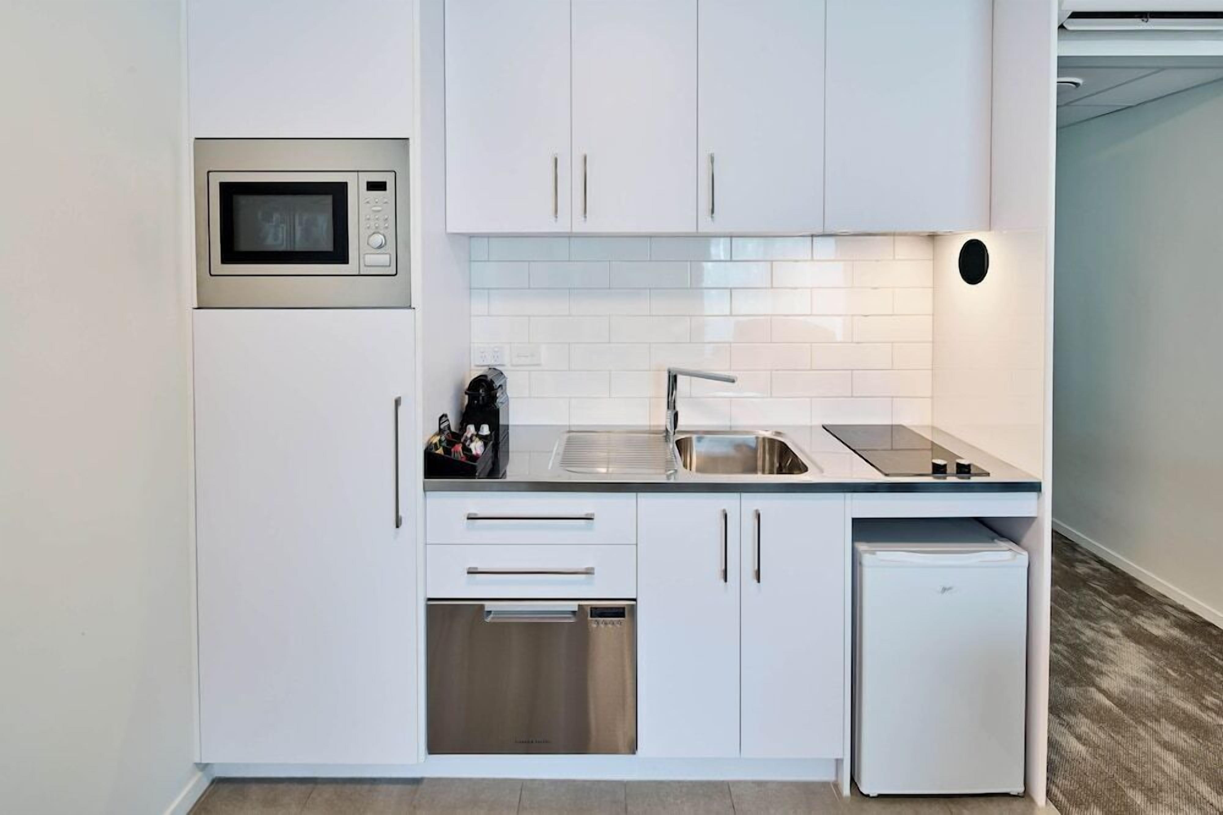 A modern kitchen with white cabinetry, a built-in microwave, a sink, and a dishwasher.