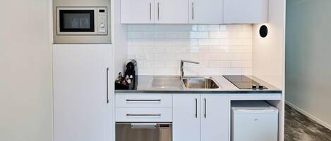 A modern kitchen with white cabinetry, a built-in microwave, a sink, and a dishwasher.