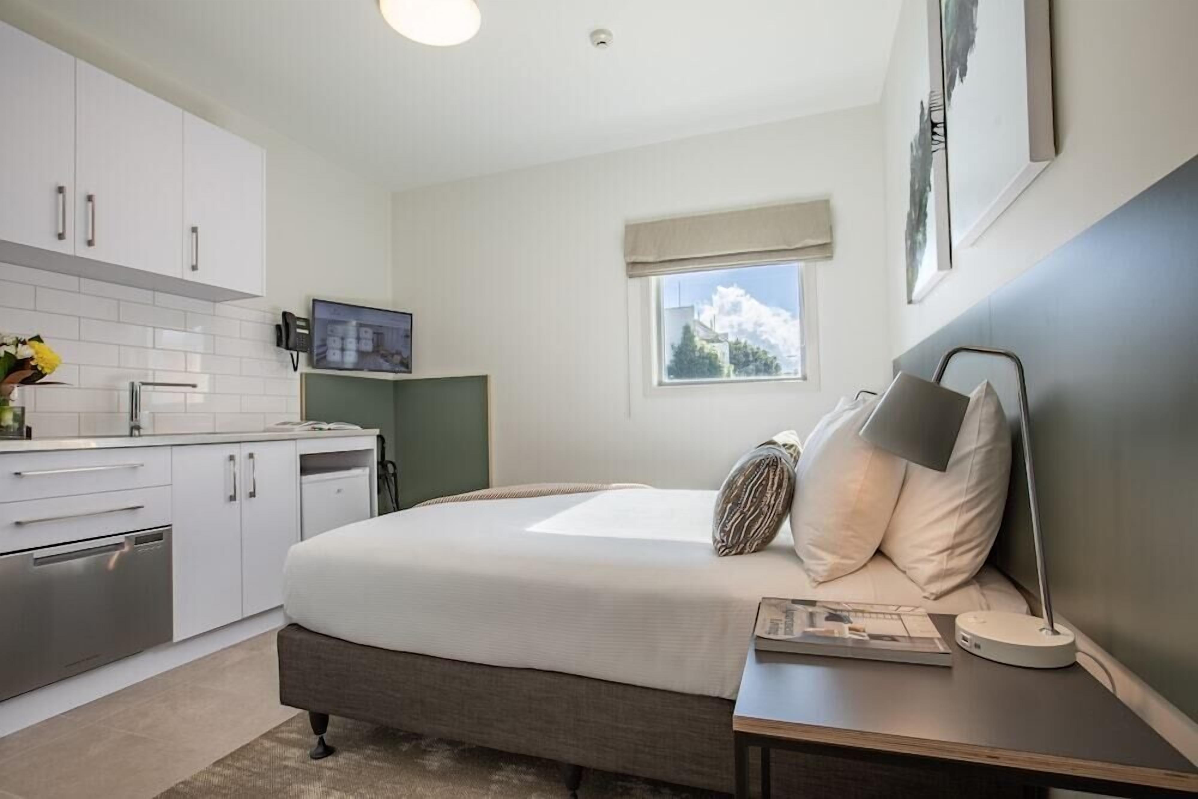 A bedroom with a bed, bedside table, lamp, and a view of the outdoors.