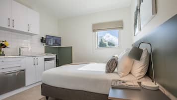A bedroom with a bed, bedside table, lamp, and a view of the outdoors.