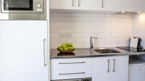A kitchen with white cabinets, a stainless steel microwave, a sink, and a bowl of green apples on the counter.