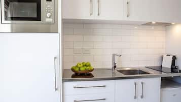 A kitchen with white cabinets, a stainless steel microwave, a sink, and a bowl of green apples on the counter.