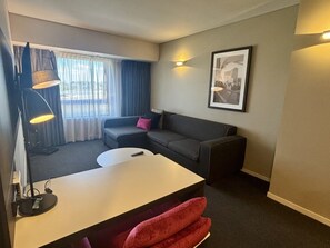 Ein kleines Hotelzimmer mit Sofa, Tisch, Lampe und einem gerahmten Bild an der Wand.