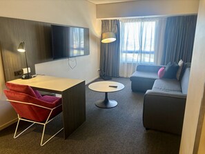 A hotel room with a desk, chair, round table, sofa, and a TV mounted on the wall. - Apartment 1112 ‘The middle of everywhere’ (Southbank)