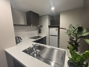 A modern kitchen with a stainless steel sink, a kettle, a refrigerator, and a potted plant. - Apartment 1112 ‘The middle of everywhere’ (Southbank)