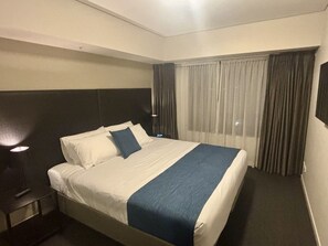 Ein Hotelzimmer mit einem Bett, einem Nachttisch, einer Lampe und einem Fenster mit Vorhängen.