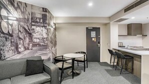 Ein modernes Hotelzimmer mit einem grauen Sofa, einem runden Tisch und einer Küchenzeile mit einer Bar.