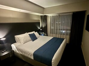 A hotel room with a bed, a nightstand, a lamp, and a window with curtains. - Apartment 1112 ‘The middle of everywhere’ (Southbank)