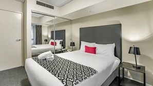Ein Hotelzimmer mit einem großen Bett, einem Nachttisch mit Lampe, einem Spiegel und einer Tür zu einem weiteren Raum.