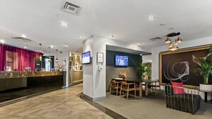 Eine Hotelhalle mit Rezeption, Sitzgelegenheiten und einem Fernsehbildschirm.