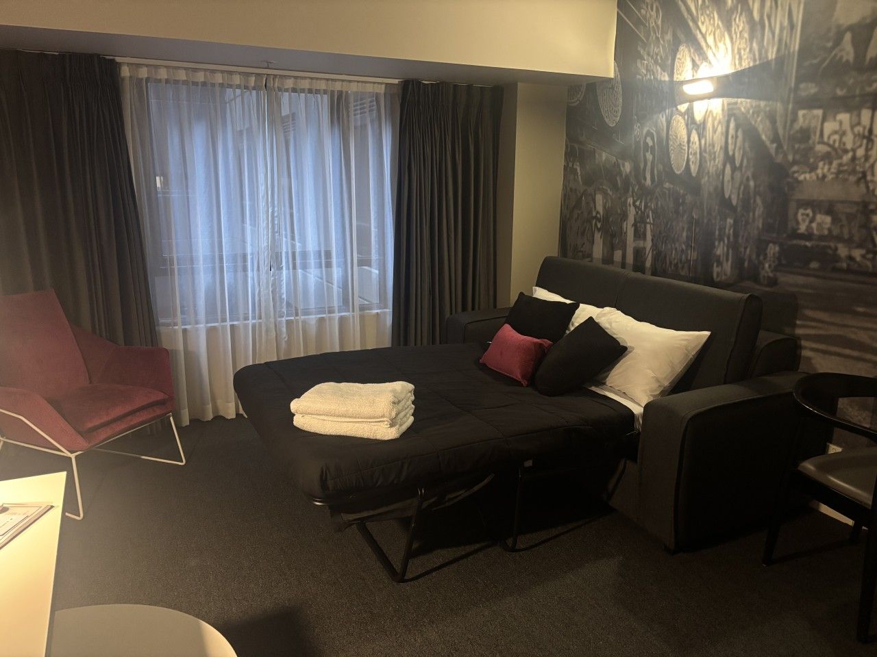 A hotel room with a bed, a chair, a desk, and a window with curtains.