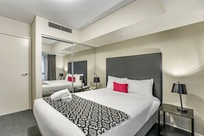 Ein Hotelzimmer mit einem großen Bett, einem Nachttisch mit Lampe, einem Spiegel und einer Tür zu einem anderen Raum.
