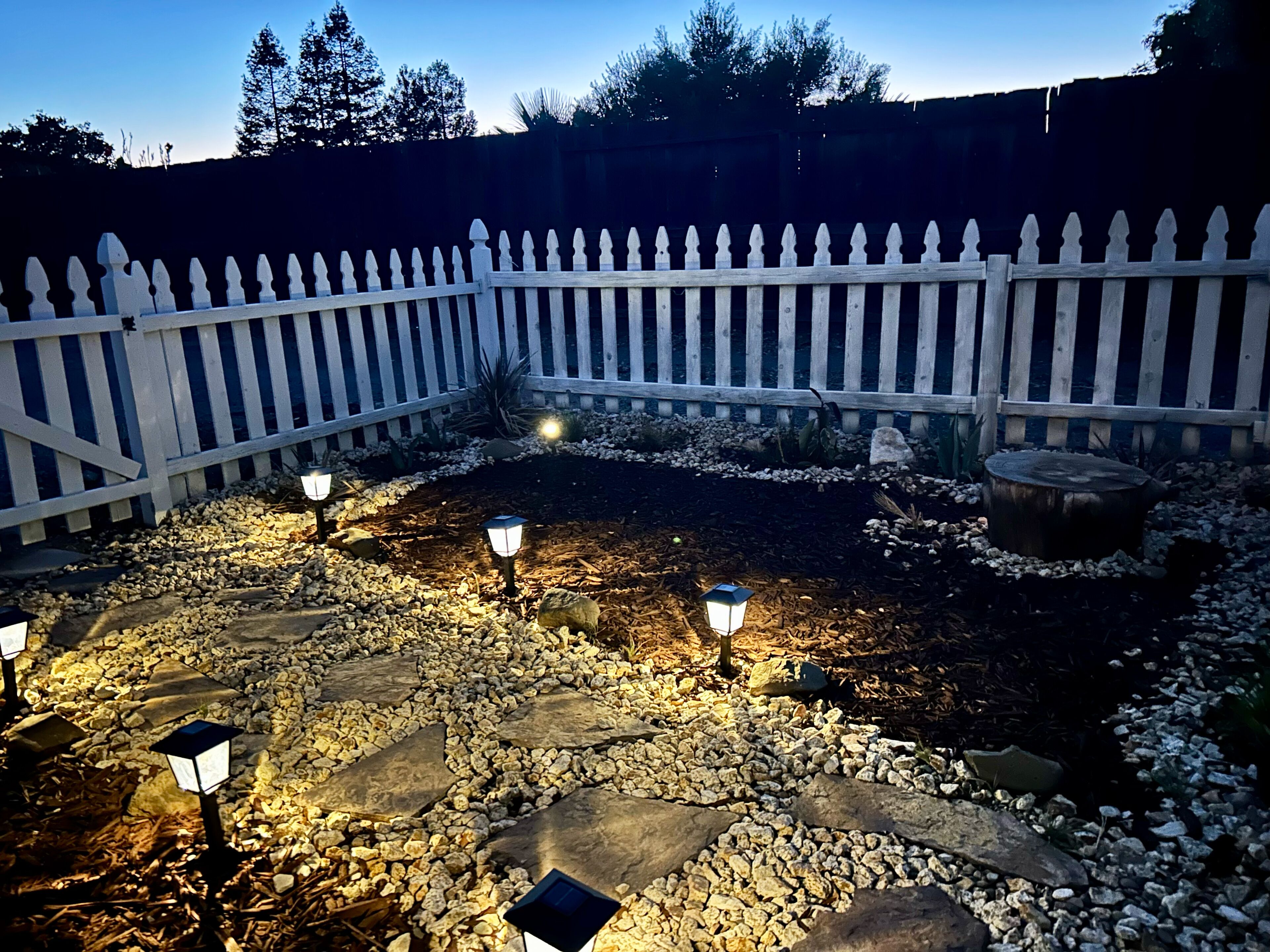 A garden area with a white picket fence, stone pathways, and solar-powered garden lights.