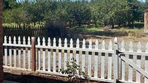 A white picket fence with a brick wall on one side and a clear blue sky in the background.
