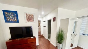 A living room with a flat-screen TV on a wooden cabinet, a potted plant, and artwork on the walls.