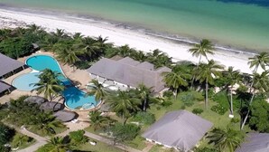 Ein Luftbild eines Resorts mit Schwimmbad, Strand und Palmen.