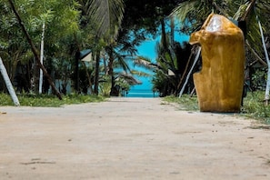 A pathway leading to a beach with a large golden statue on the right. - JAZ Elite Adonia (Uroa)