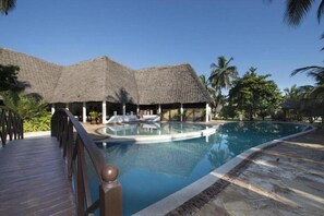 A pool area with a wooden deck and thatched-roof structures. - JAZ Adonia Beach Resort (Uroa)