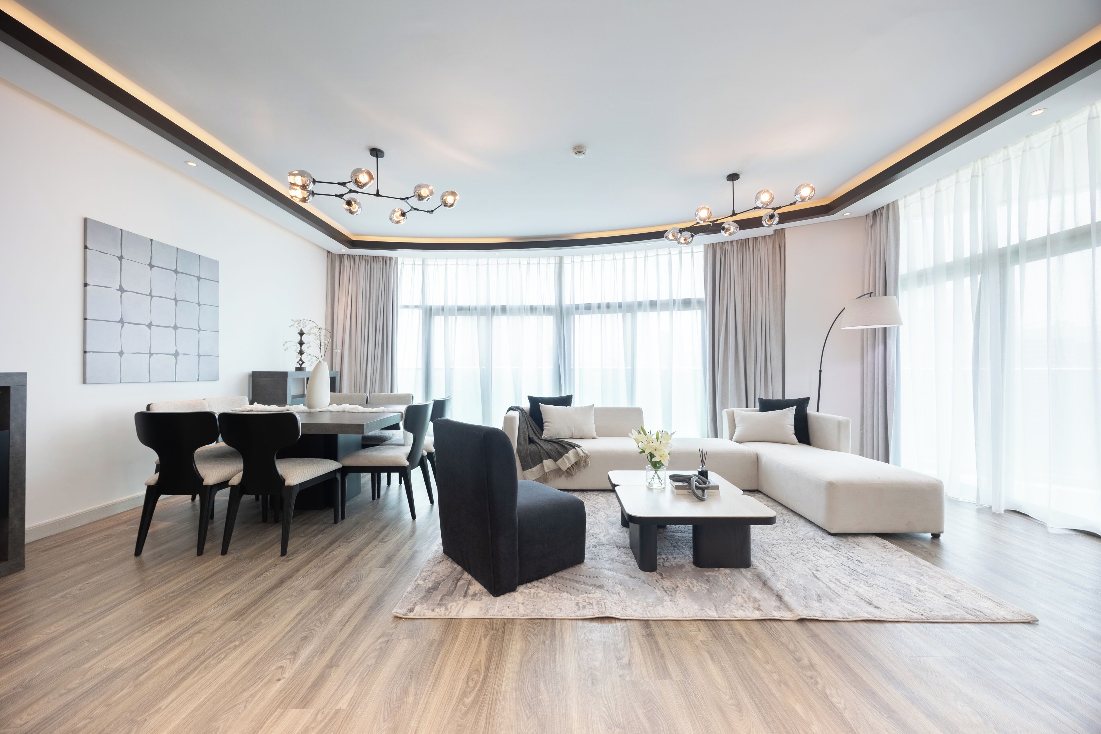 A modern living room with a dining area, featuring a sofa, chairs, a coffee table, and a chandelier.