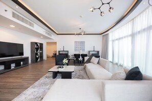 A modern living room with a large flat-screen TV, a sofa, a coffee table, and a dining area with chairs and a table. - Bloomfields 3BR plus Maid in Beach Tower (Abu Dhabi)