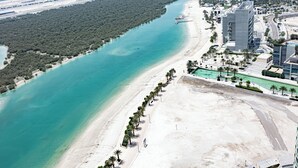 An aerial view of a coastal area with a beach, a river, and a cityscape with modern buildings. - Bloomfields 3BR plus Maid in Beach Tower (Abu Dhabi)