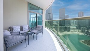 A balcony with a seating area, a glass railing, and a cityscape view. - Bloomfields 3BR plus Maid in Beach Tower (Abu Dhabi)