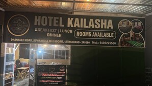 Un cartel del Hotel Kailasha que anuncia servicios de desayuno, almuerzo y cena, con un número de contacto y disponibilidad de habitaciones.