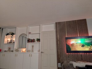 Ein Wohnzimmer mit Fernseher, weißen Schränken, einem Spiegel und einer Tür.