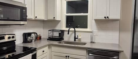 A modern kitchen with white cabinets, stainless steel appliances, a black faucet, and a window above the sink.