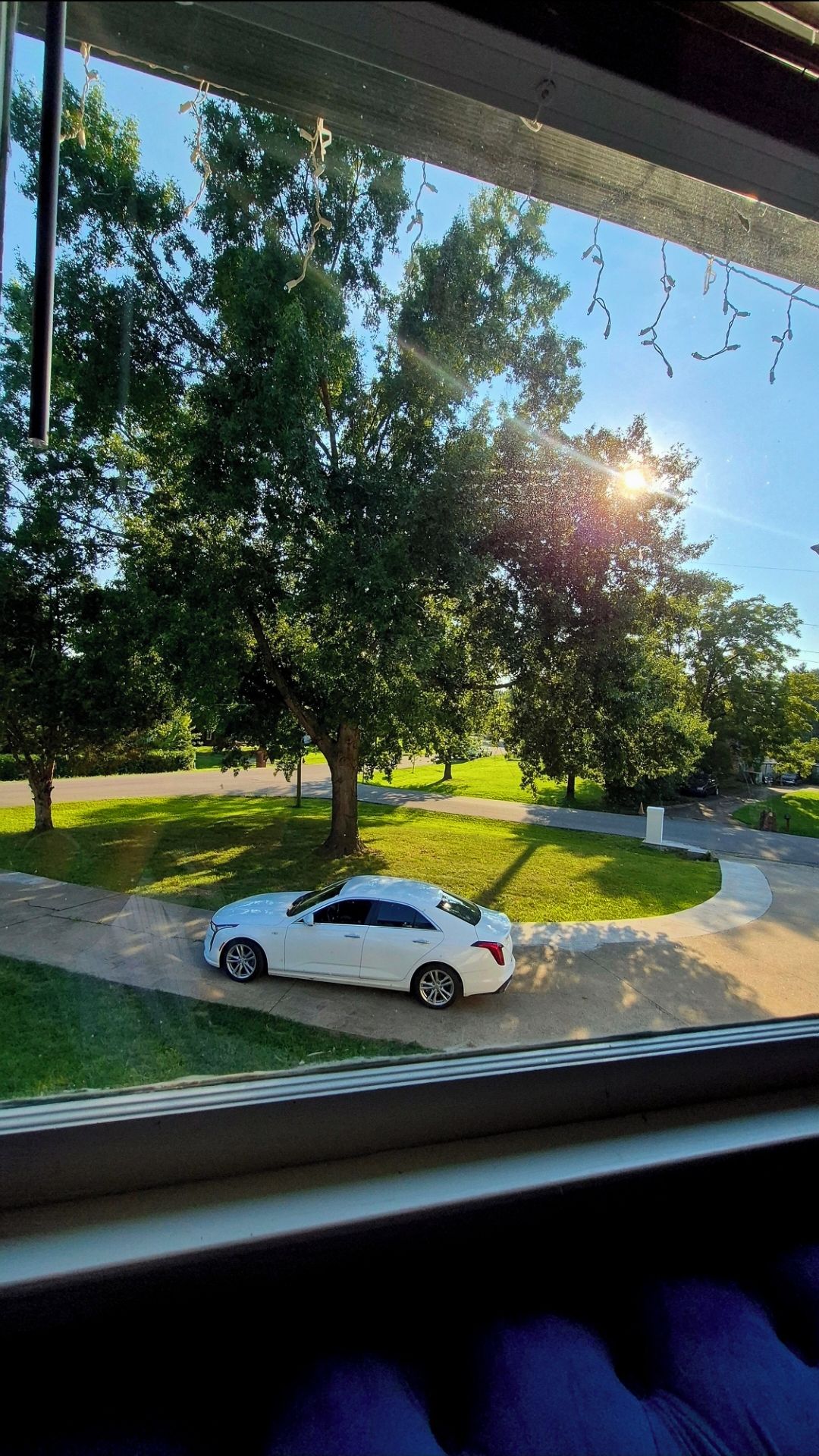 A white car parked on a driveway with trees and a clear sky in the background.