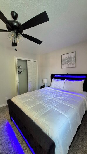 Ein Schlafzimmer mit einem Bett, einem Deckenventilator, einem Nachttisch mit Lampe und einer Tür mit Schrank.
