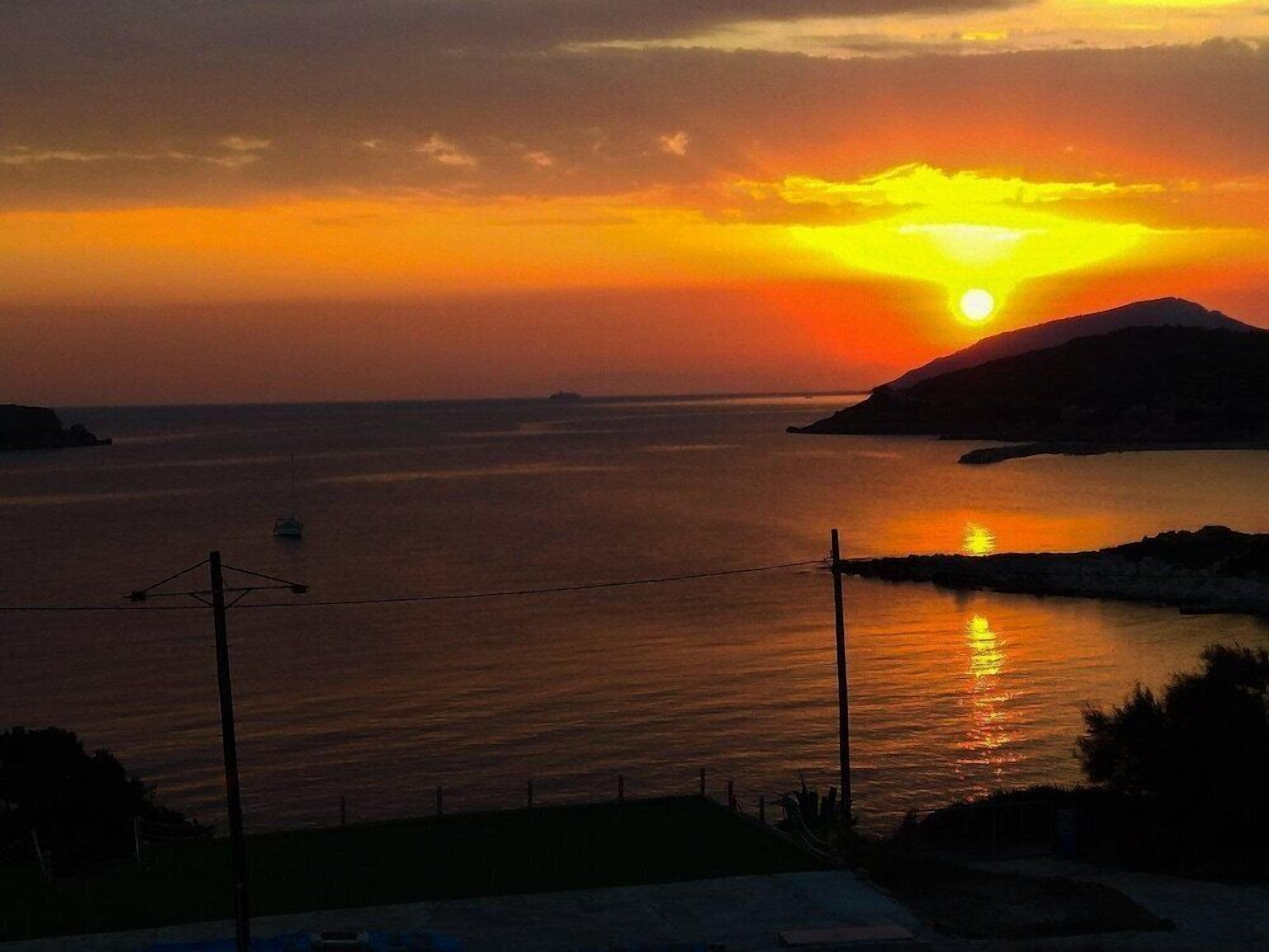 Un atardecer sobre una masa de agua, con la silueta de tierra en la distancia.