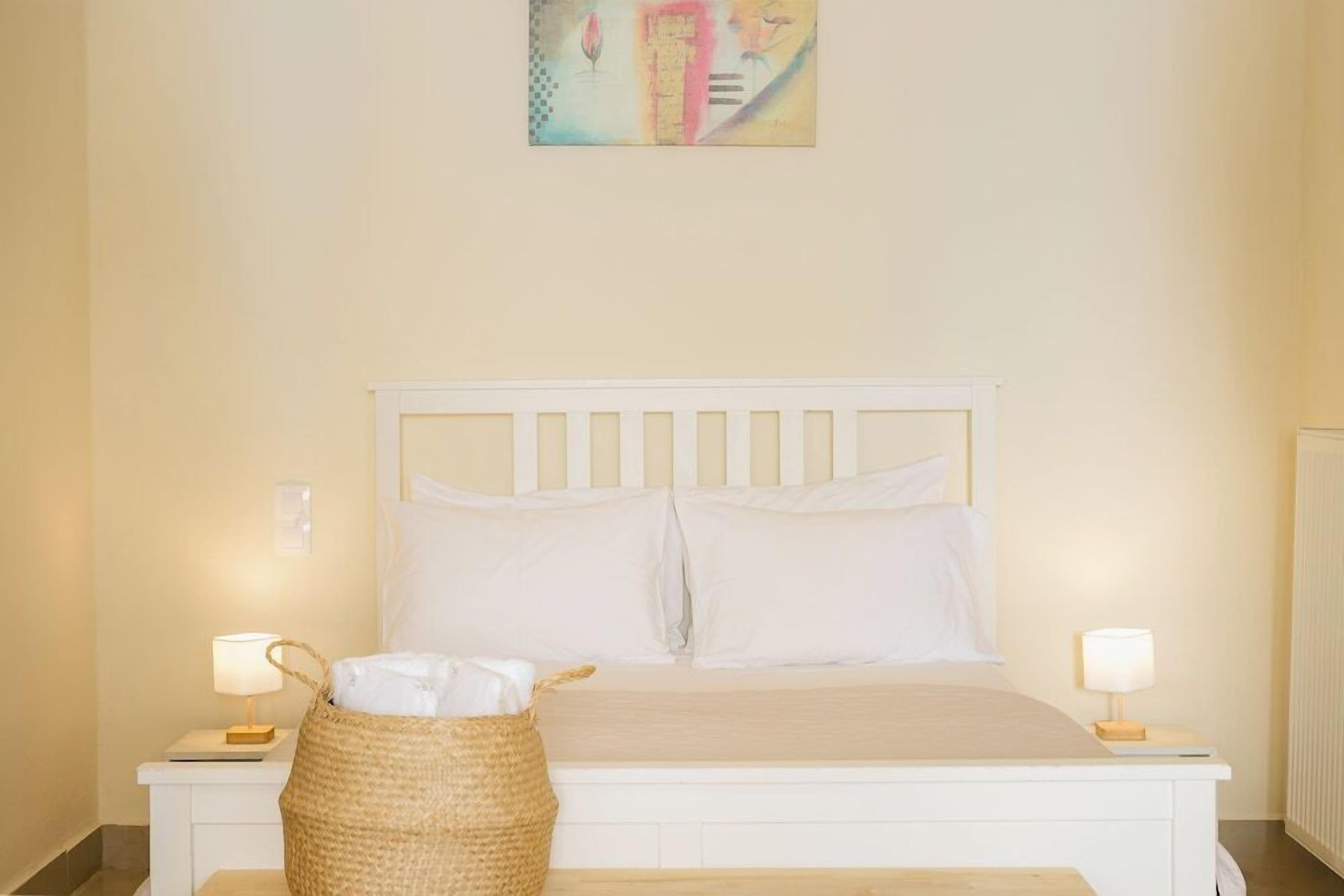 A bedroom with a white bed, two bedside lamps, a bedside table, and a woven basket on the floor.