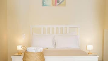 A bedroom with a white bed, two bedside lamps, a bedside table, and a woven basket on the floor.